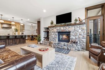 A spacious and inviting open-concept living room and kitchen in Highlands Lodge 205, featuring a large stone fireplace, comfortable leather seating, and modern kitchen amenities.