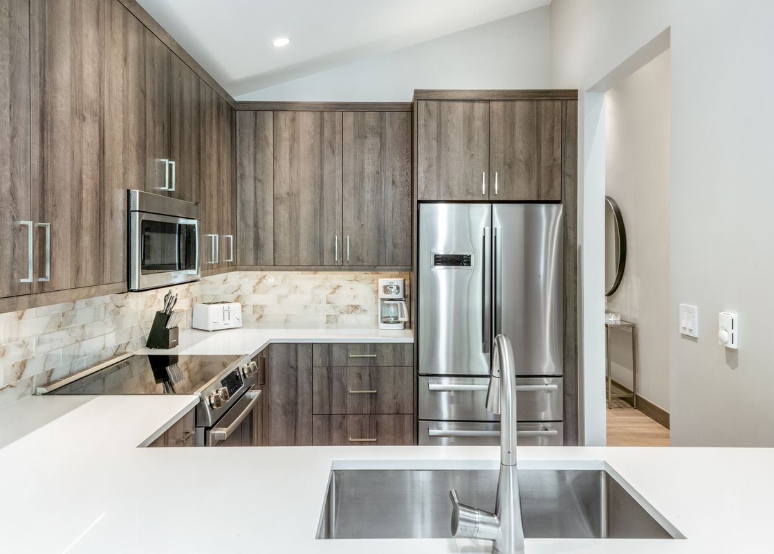 A modern kitchen with wood cabinets, stainless steel appliances, and white countertops.