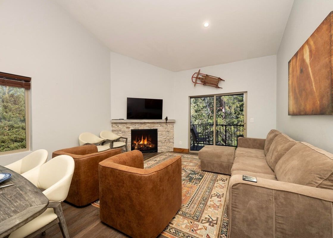 A spacious living room at Vasquez Creek Townhomes 8 features a comfortable sectional sofa, two armchairs, a large area rug, and a fireplace, with a view of the forest through the windows.