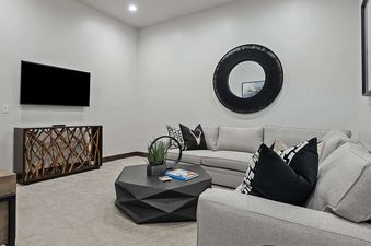 The contemporary living space at Retreat at Black Rock Ridge features a comfortable L-shaped sofa, a sleek geometric coffee table, and a wall-mounted TV above a unique console table, creating a perfect blend of style and comfort.
