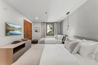 A modern guest room at Alpine at the Ritz Carlton featuring two queen-sized beds and a wall-mounted TV.