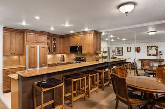 A spacious kitchen and bar area in Montaneros 204 featuring wooden cabinets, granite countertops, modern appliances, and a bar with animal hide upholstered stools next to a round dining table.