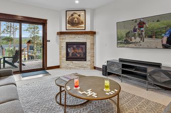 The living room of the Cherrybrook Chalet features a cozy fireplace, a large TV, and comfortable seating with sliding glass doors opening to an outdoor view.