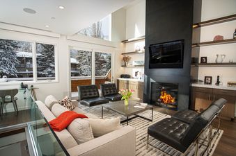 A modern and cozy living room with a fireplace, comfortable seating, and large windows looking out onto a snowy landscape.