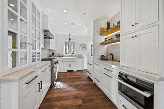A modern kitchen with white cabinetry, dark hardwood floors, stainless steel appliances, and a window above a large sink.