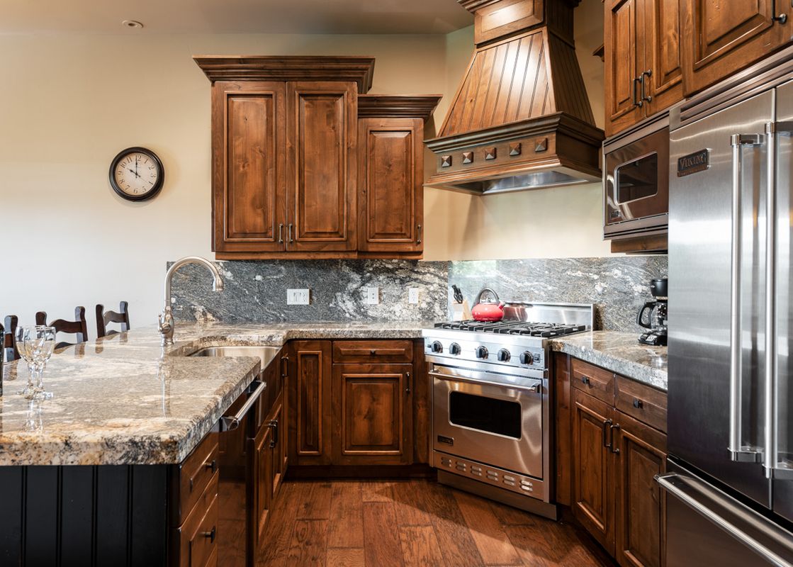 A gourmet kitchen with dark wood cabinets, granite countertops, and stainless steel appliances at 103 Juniper Landing.