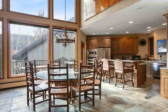 The Pinnacle 1358's kitchen and dining area features a glass-top table with wooden chairs, rich wooden cabinetry, stainless steel appliances, and large windows with outdoor views.