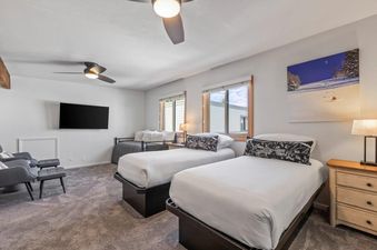 A spacious bedroom at Snow Flower 79 Park City featuring two twin beds with white linens, a nightstand, and a wall-mounted TV, along with a comfortable seating area.
