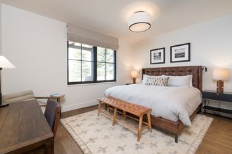 A bedroom with a king-sized bed, a wooden bench, and a window with a view of trees.