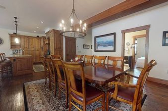 A spacious dining area with a large wooden table and chairs, adjacent to a kitchen with wooden cabinetry, all under a chandelier in The Landmark 4 Bedroom 4 Bathroom Penthouse.