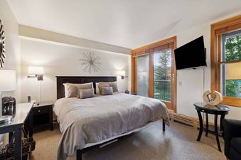 A bedroom with a king-sized bed and a view of the forest from the patio door.