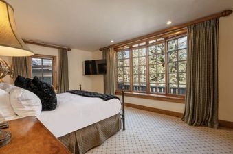 The bedroom in Chalet 12 features a large bed with a dark throw and pillows, positioned opposite a wall-mounted flat-screen television.