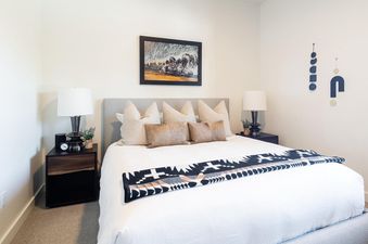 The bedroom in Moonlight Basin 6A Treeline Springs features a king-size bed with a white duvet and a patterned throw blanket, a set of white, brown, and cream throw pillows, and two bedside tables with lamps.