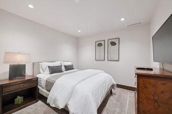 The bedroom at Riverfront Townhome 10 is elegantly furnished with a queen-sized bed, a rustic wooden nightstand with a lamp, and two botanical prints, offering a comfortable and stylish retreat.