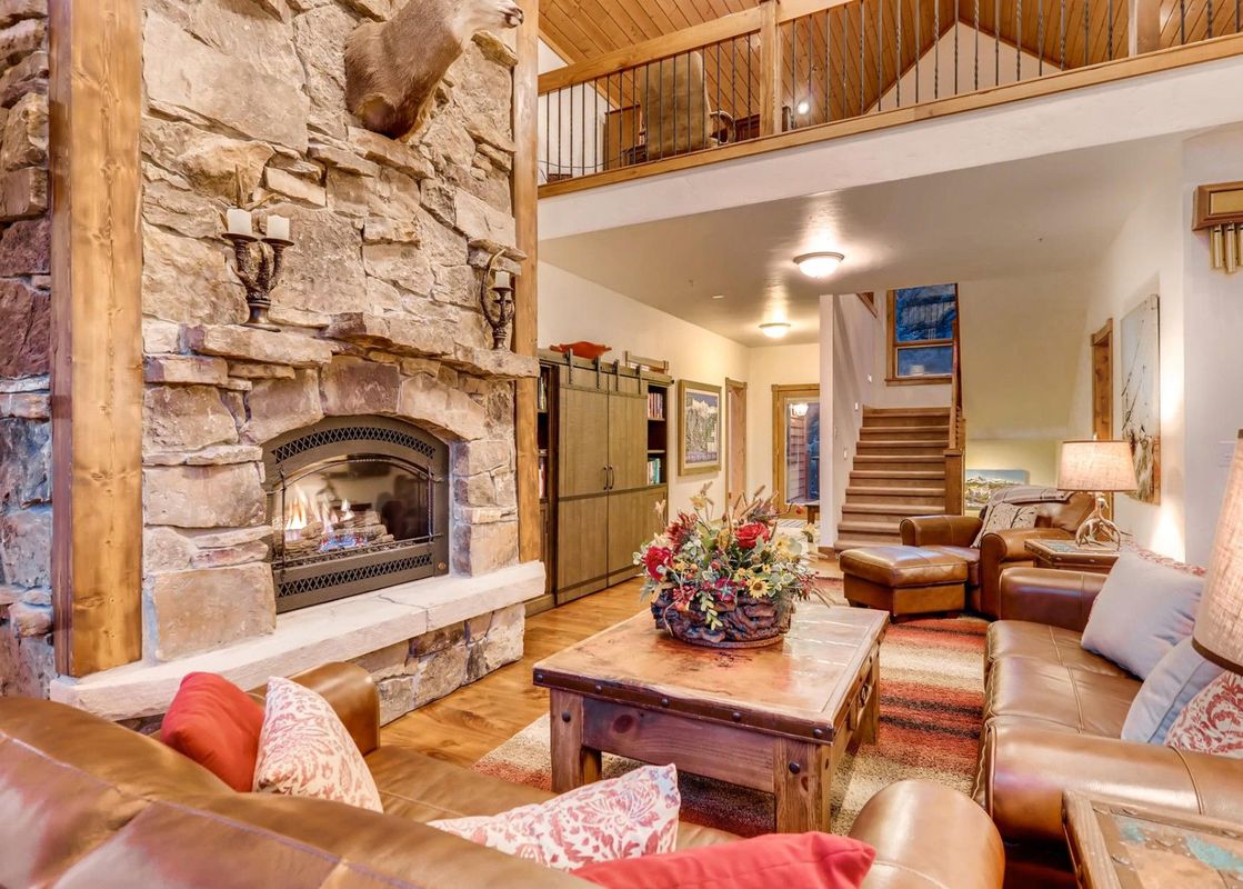 The Timber Creek Retreat at River Ridge features a spacious living area with a stone fireplace, leather sofas, and a rustic wooden coffee table.