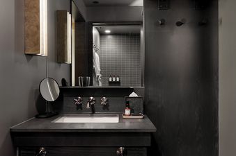 A sleek, modern bathroom vanity area in Mollie Aspen Snug King features a white sink, brass fixtures, and a large mirror reflecting a tiled shower with bathrobes.