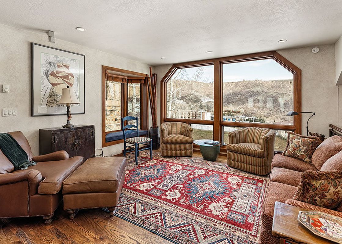 A cozy living room in Woodrun V Residence 5, featuring a large rug, a comfortable sectional sofa, and expansive windows offering scenic mountain views.
