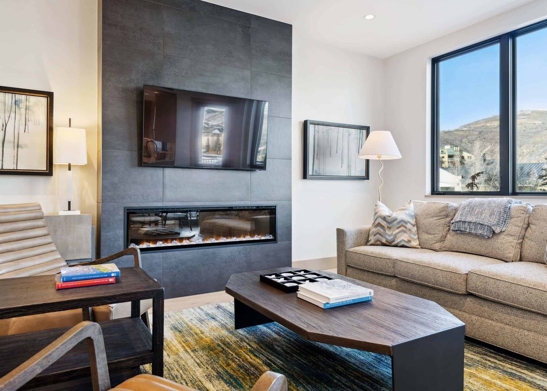 One Riverfront Condo 203 living room features a fireplace, a large flat screen TV, a sofa, two chairs, and a coffee table.