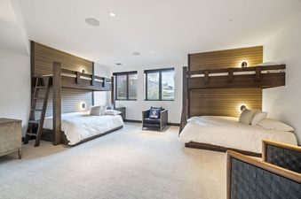 A bunk room at Alpine Opus with two sets of wooden bunk beds, featuring white bedding, reading lights, and large windows revealing an outdoor landscape.