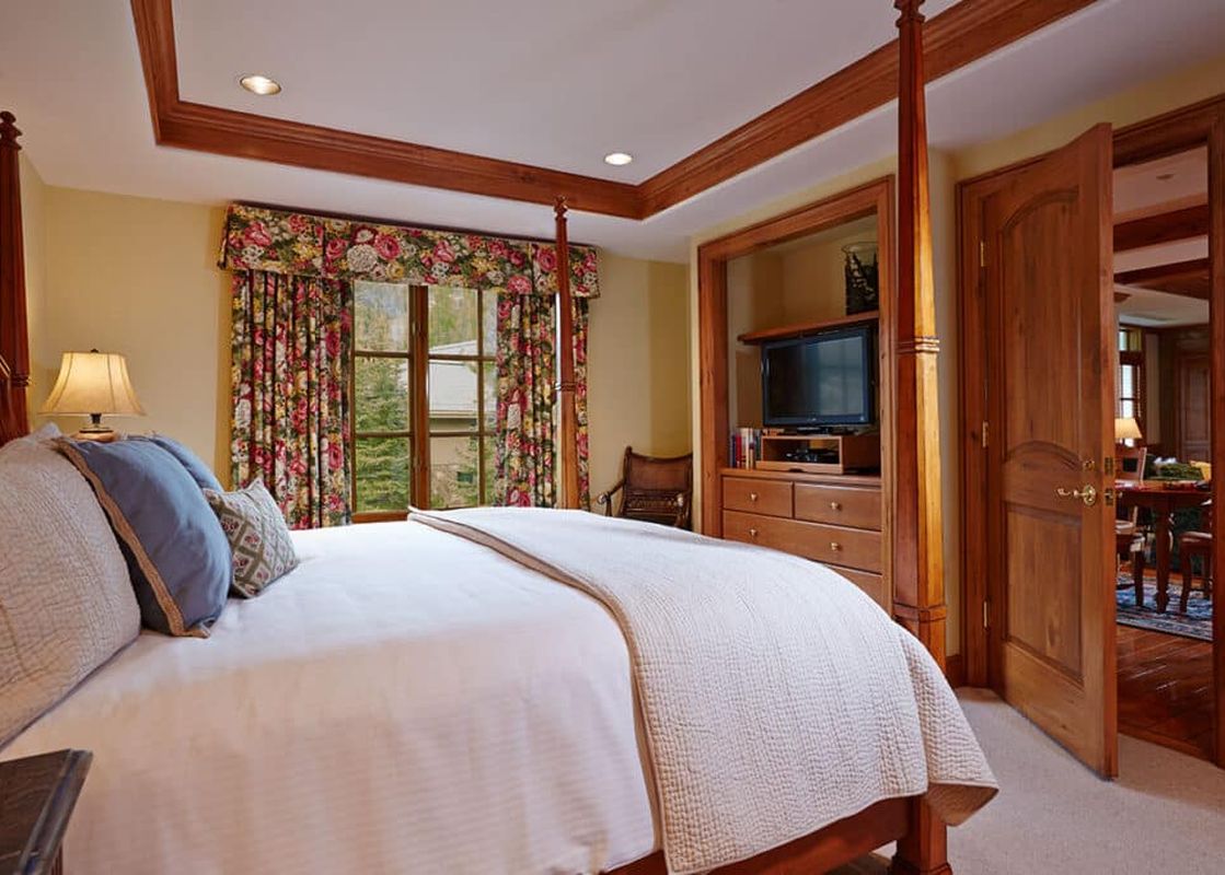 A warm and inviting bedroom with a four-poster bed, floral curtains, and a television cabinet, offering comfort and entertainment within Chateau Beaver Creek Residence 305.