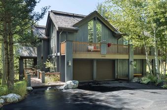 Exterior view of Teton Grove with a wooden deck, a two-car garage, and lush green trees.