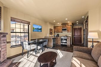 A wide-angle shot of the living area at Copperbottom Inn 104, showcasing the dining area by the window, the fully equipped kitchen, and the inviting lounge space with a fireplace.
