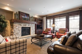 A cozy living room with a stone fireplace, plush seating, and large windows offering a winter view at Silver Star 902.
