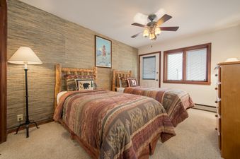 A rustic-themed guest bedroom with two twin beds, log frames, textured feature wall, and natural light at Teewinot C5.