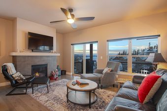 The living area of Rendezvous 47 Lookout Point boasts comfortable seating around a fireplace and a large television, with expansive windows offering views of the snowy landscape outside.
