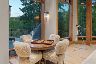 A cozy game area in Silver Creek Lodge, featuring a wooden table with backgammon, surrounded by four plush, cream-colored chairs, all set against a backdrop of large windows offering stunning views of a lush, tree-filled landscape.