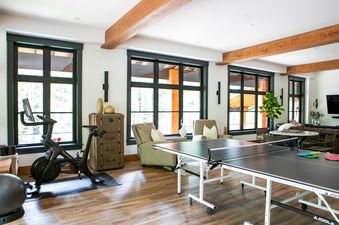 A bright and spacious games room at Falcon Cottage featuring a black ping pong table, a Peloton exercise bike, and comfortable seating near large windows.