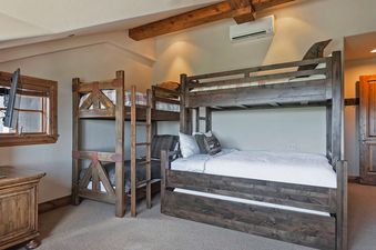 A cozy bunk room at the Retreat at Empire Pass, featuring sturdy wooden bunk beds with comfortable bedding and an entertainment setup, perfect for a family or group stay.