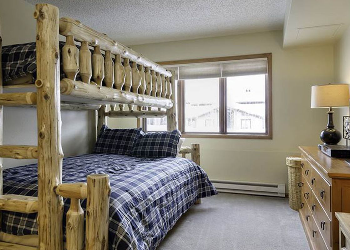 A rustic bunk room with a log bunk bed and blue plaid bedding, accompanied by a wooden dresser with lamps and a TV, offers a cozy retreat in the Ranch at Steamboat RA405.