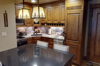 A kitchen with dark wood cabinets, a black granite countertop, and two bar stools.