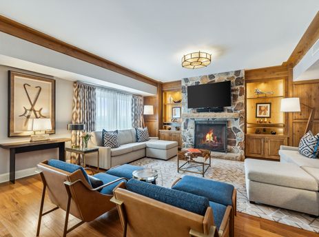 A spacious and inviting living room in the St Regis Executive Suite features a large stone fireplace, a comfortable sectional sofa, and elegant wooden furnishings.
