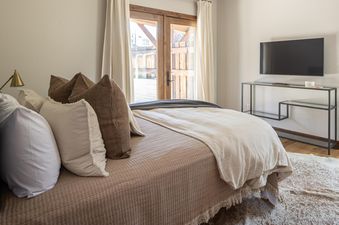 A serene bedroom featuring a large bed with multiple pillows, a flat-screen TV, and a door leading outside.