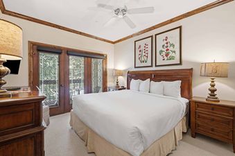 A spacious bedroom at The Charter G230 with a large bed, wooden furniture, botanical wall art, and French doors leading to an outdoor view.