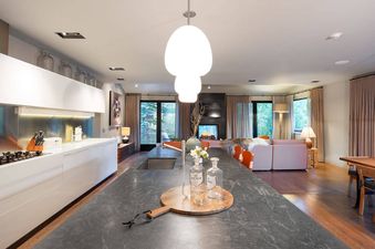 A modern open-plan living area and kitchen at Riverbend House with white cabinetry, a dark grey island, and a distant fireplace with seating.