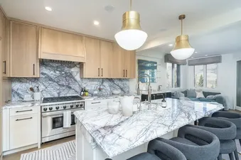 A modern kitchen at Lorian Rise with light wood cabinetry, white marble countertops, a stainless steel stove, and a large island with bar stools.
