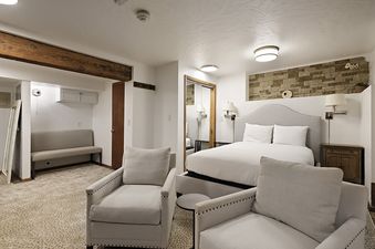 A cozy bedroom area in Fasching Haus Unit 13 features a king-sized bed, two armchairs, and a small sitting area with a bench, all under warm lighting.
