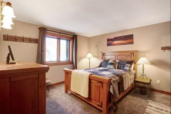A cozy bedroom with a wooden bed frame, plaid bedding, and a large window with natural light.