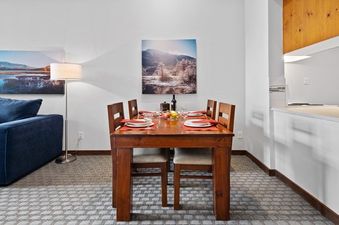 The image features a dining area with a wooden table set for six, a blue sofa, and a floor lamp, creating a cozy and inviting atmosphere.