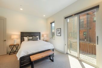 A modern bedroom with a large bed, two side tables with lamps, and a private balcony overlooking the surrounding area.