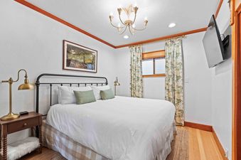 The cozy bedroom at Woodside Cottage features a comfortable bed with a white duvet and green pillows, a bedside table with a lamp, and a window with curtains.