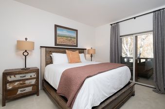 A bedroom with a queen-sized bed, a wooden headboard, and a view of the mountains from the window.