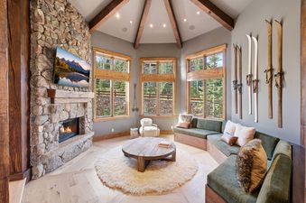 Living area with stone fireplace, wooden details, curved sectional sofa, and vintage skis on the wall.