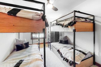 A cozy bunk room at BlueSky Breckenridge 504 features two modern bunk beds with black metal frames and wood accents, soft bedding, decorative pillows, a ceiling fan, and a window with an exterior view.