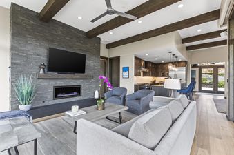 A modern open-concept living room with a grey sofa, blue armchairs, and a fireplace, connected to a kitchen with dark wood cabinets and a kitchen island.