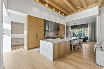 A modern kitchen in Kestrel at the Colony featuring light wood cabinetry, a large marble island with a sink, and a view of lush greenery outside.