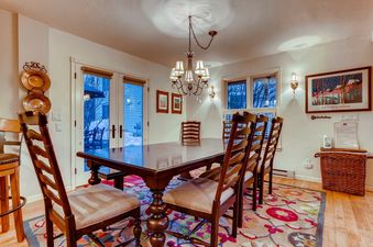 The dining room at Chalet Montagne features a large wooden table with matching chairs and elegant lighting, leading to an outdoor area visible through glass doors.